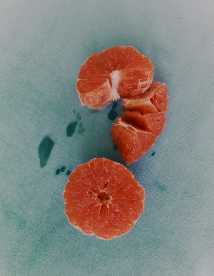 Peeled red grapefruit segments on a pale teal surface