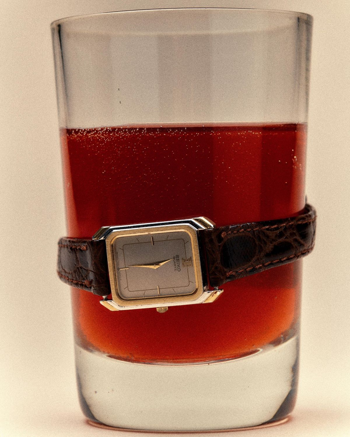 A vintage watch wrapped around a glass of deep-red liquid